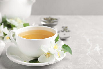 Cup of tea and fresh jasmine flowers on light grey marble table. Space for text