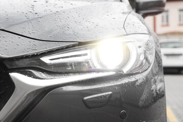 Car with switched on tail light in drops of water outdoors, closeup