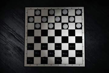 Checkerboard with game pieces on black table, top view