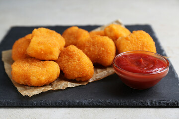 Tasty chicken nuggets with ketchup on light grey textured table, closeup