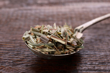 Fototapeta na wymiar Metal spoon with aromatic dried lemongrass on wooden table, closeup