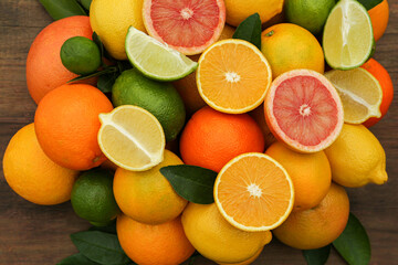 Different citrus fruits with green leaves on wooden table, flat lay