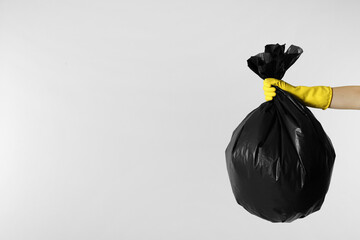 Janitor in rubber glove holding trash bag full of garbage on light grey background, closeup. Space...