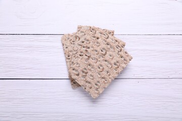 Fresh crunchy crispbreads on white wooden table, top view