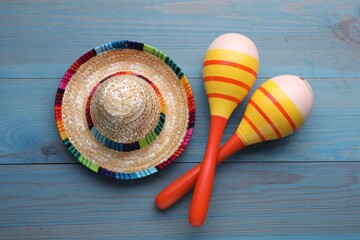 Colorful maracas and sombrero hat on light blue wooden table, flat lay. Musical instrument