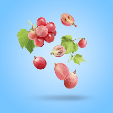 Delicious fresh red grapes and green leaves falling on light blue background