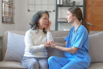 Portrait of attractive young caucasian female nurse elderly caregivers with senior patient home caring for elderly asia female patients on couch, indoors. hand clasp to encourage