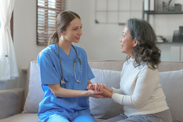Obraz premium Portrait of attractive young caucasian female nurse elderly caregivers with senior patient home caring for elderly asia female patients on couch, indoors. hand clasp to encourage