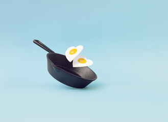 Creative idea with a frying pan and a two fried eggs in heart shape on a bright blue background. Minimal food and love concept. Breakfast idea for Valentine's day and romantic morning. Copy space.
