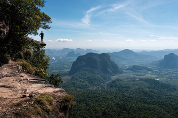 A tourist stands on the cliff overhanging the plain on sunny day. Dragon's Crest (Khao Ngon Nak) Viewpoint, Krabi Province, Thailand.