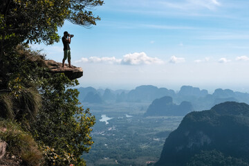 A photographer tekes picture from cliff edge overhanging the plain on sunny day. Dragon's Crest (Khao Ngon Nak) Viewpoint, Krabi Province, Thailand.
