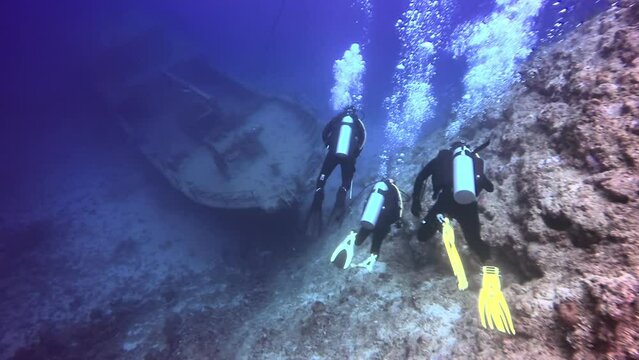 Group of divers swims near ship wreck underwater. Sunken ship covered in coral on Pacific Ocean seabed in Fiji.