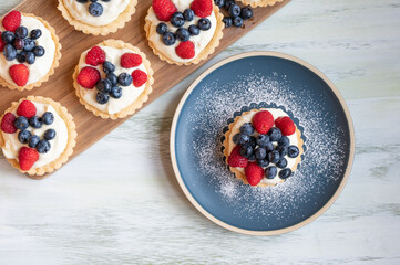 Small tarts filled with custard and berries on a white table.