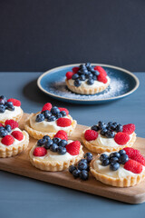 Blueberry and raspberry topped small tarts and a blue plate on a blue table.
