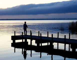 Fototapeta na wymiar A Single Fisherman Stands on the Dock Fishing in Pre Dawn Light