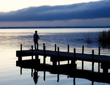A Single Fisherman Stands on the Dock Fishing in Pre Dawn Light