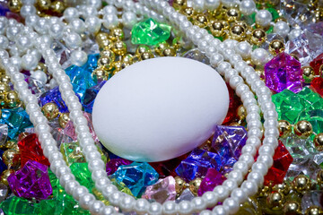 Looking down at a white chicken egg surrounded by colorful beads and treasure. Copy space. 