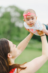 Young adult woman looking up and holding baby girl 
 above head with child looking at camera