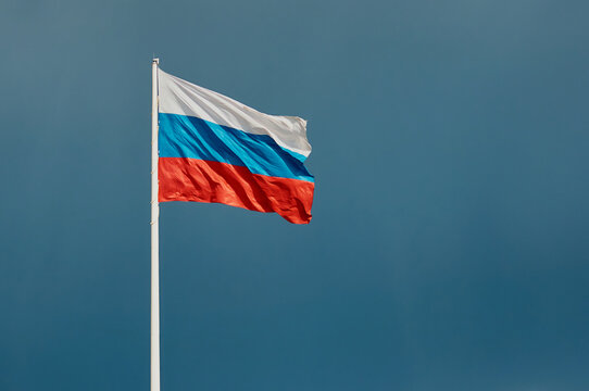 Russian flag against a dark blue sky with empty space for text. The state flag of the Russian Federation, 75 meters high, flutters in the wind. Built-in anemometer and emergency flag lowering system.