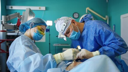 Female nurse hold the lifted skin of a patient with a metal tool. Surgeon applies instruments in the breast cavity preparing place for implant.