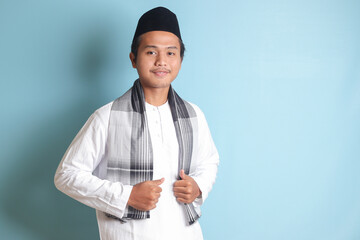 Portrait of Asian muslim man in white koko shirt feeling confident, smiling and looking at camera. Isolated in blue background - obrazy, fototapety, plakaty