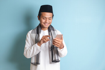 Portrait of young Asian muslim man holding mobile phone with smiling expression on face. Isolated image on white background