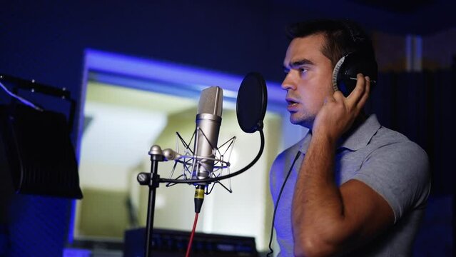 Male Caucasian singer performing song in the modern studio. Man sings a lyrical composition and then starts laughing.