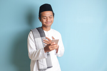 Portrait of young Asian muslim man holding mobile phone with smiling expression on face. Isolated...