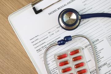 Blank sheet of patient's medical history form with stethoscope and pills, top view.