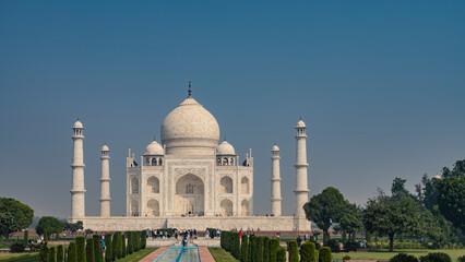 Fototapeta na wymiar Beautiful white marble ancient Taj Mahal against the blue sky. Symmetrical mausoleum with domes, arches, minarets. Many people admire the shrine. India. Agra.