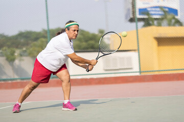Active senior woman playing tennis on court.