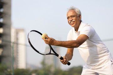 Senior man with racket and ball on tennis court.