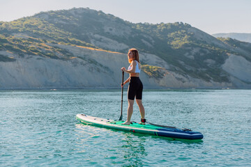 Young woman rowing on stand up paddle board at quiet sea with beautiful landscape.