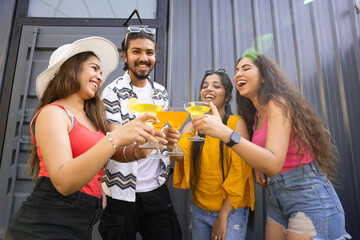 Group of cheerful young indian friends drink cocktails having fun together. Happy people talking...