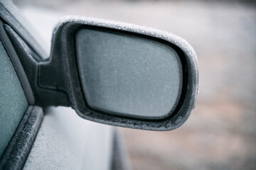 Car parked outside during the winter season. Macro shot of a side view mirror is covered with a thin layer of ice. Frosty morning.