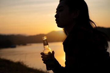 Asian silhouette woman holding beer bottle on the beach at sunset