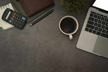 Laptop computer, coffee cup, calculator and notebook on black slate stone background. Flat lay, Top view