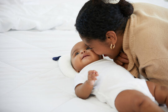 African young mother kissing her infant baby lying on the bed