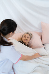 Obraz na płótnie Canvas Caregiver for an elderly woman blanket the elderly woman on the bed After completing the weekly health check-up at the patient's home