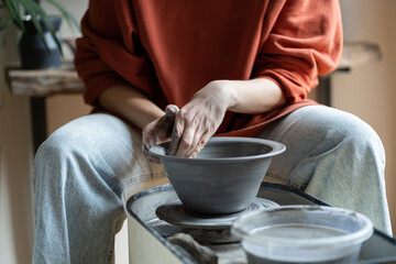 Fototapeta na wymiar Hands of creative woman sculpture working with potter wheel during production of handmade utensils. Close-up of process of creating clay plate for serving dishes by artisan running small business 