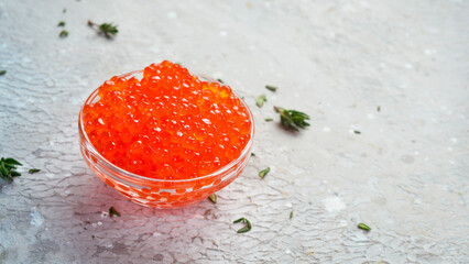 Red caviar in a glass bowl. Macro photo. On a gray concrete background. Side view.