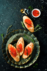 Toasts with red caviar on a stone plate, caviar in a bowl. On a black stone background. Rustic style.