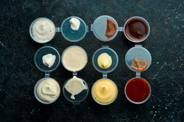 Set of sauces. Ketchup, mayonnaise, tartar, chili, and mustard sauces in plastic containers. Takeaway food. On a black stone background. Rustic style.