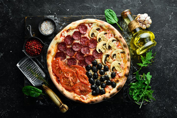 Homemade pizza with sausages, mushrooms, olives and tomatoes. Takeaway food. Home delivery of food. On a black stone background.