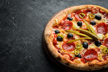 Delicious homemade pizza with pepperoni and vegetables. Home delivery of food. On a black stone background.