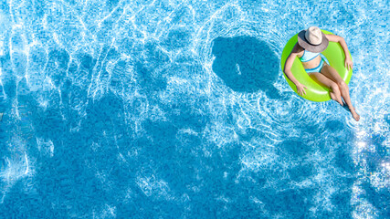 Active young girl in swimming pool aerial top view from above, teenager relaxes and swims on inflatable ring donut and has fun in water on family vacation, tropical holiday resort
