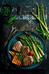 Juicy Veal steak with asparagus, tomatoes and toast. On a black stone background. Top.