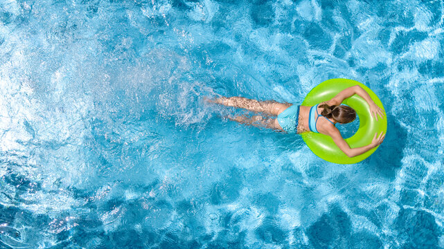 Active young girl in swimming pool aerial top view from above, teenager relaxes and swims on inflatable ring donut and has fun in water on family vacation, tropical holiday resort
 - Powered by Adobe