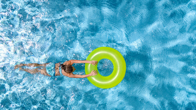 Active young girl in swimming pool aerial top view from above, teenager relaxes and swims on inflatable ring donut and has fun in water on family vacation, tropical holiday resort
