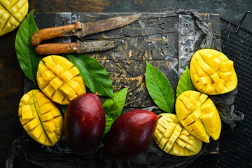 Fresh tasty sweet mango with leaves on old wooden dark background. Rustic style. Top view. Tropical fruits.